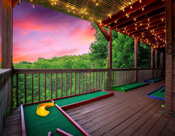A wooden deck with a green artificial turf table, a yellow table tennis table, and a green pool table.