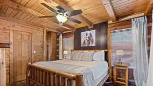 A wooden cabin bedroom with a bed, ceiling fan, and a painting on the wall.