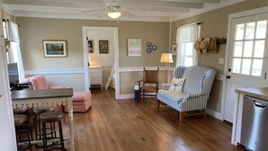 A cozy kitchen with wooden floors, a striped armchair, and a dining area with a pink sofa and stools.