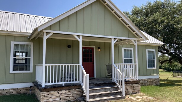 A single-story house with a front porch, a red door, and a stone foundation.