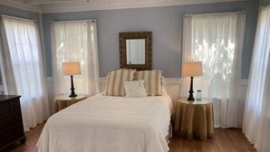 A bedroom with a large bed, two bedside tables with lamps, a dresser, and a mirror on the wall.