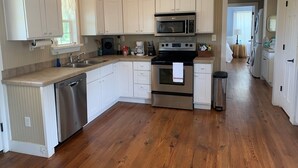 A modern kitchen with white cabinets, stainless steel appliances, and a wooden floor.
