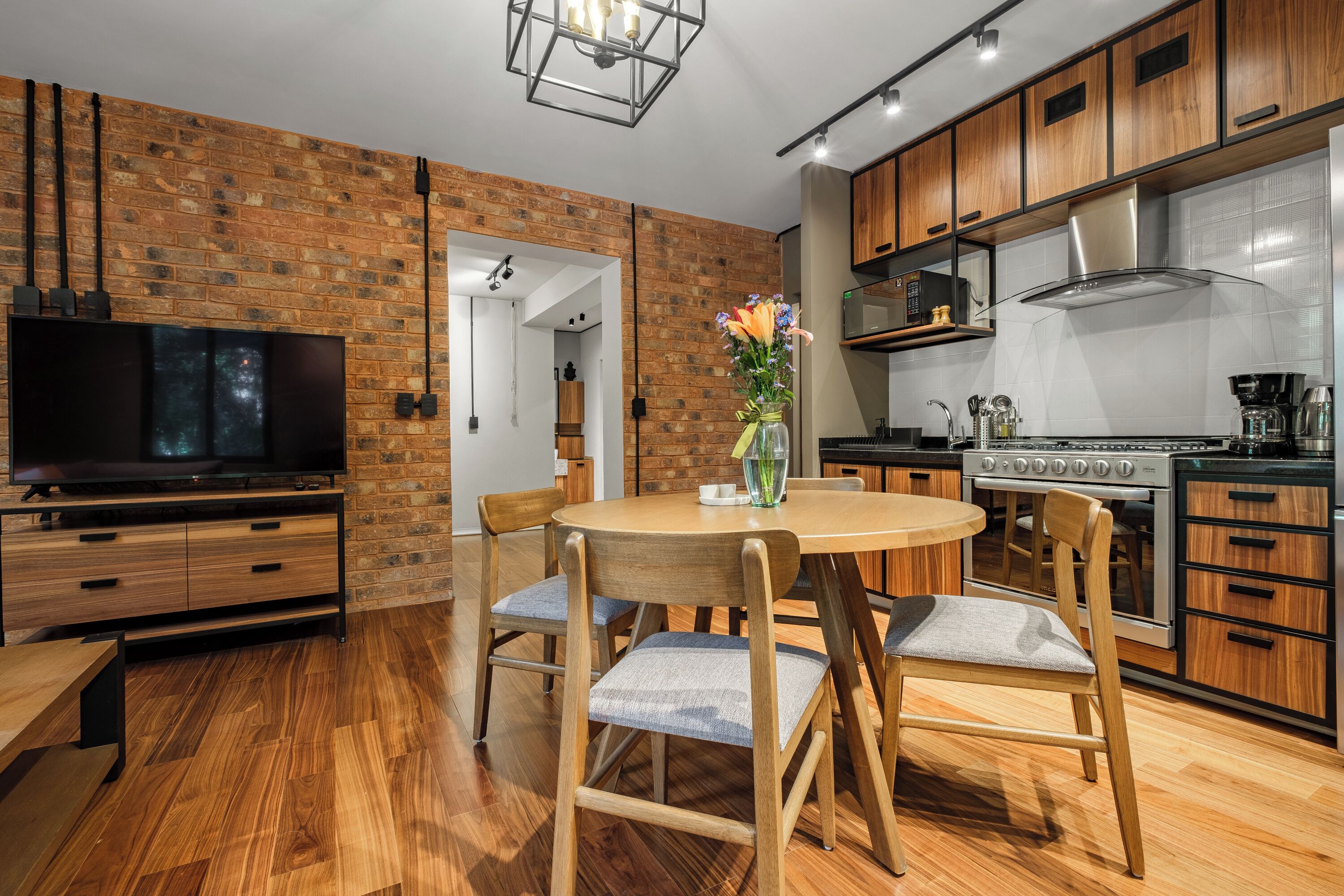 A modern kitchen with wooden cabinets, a built-in stove, and a dining area with a round table and chairs.