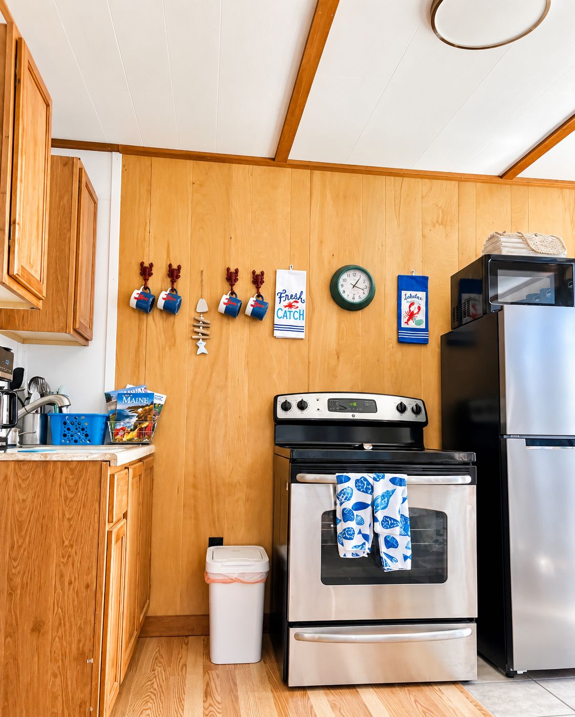 Une cuisine de taille réduite, avec des meubles de rangement en bois, une cuisinière, un four, un réfrigérateur et une horloge au mur.
