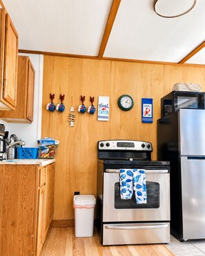 A compact kitchen with wooden cabinets, a stove, an oven, a refrigerator, and a clock on the wall.