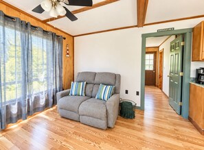 A cozy room with a grey sofa, wooden flooring, a ceiling fan, and a view of a wooden door labeled 'Moosehead Lake'.