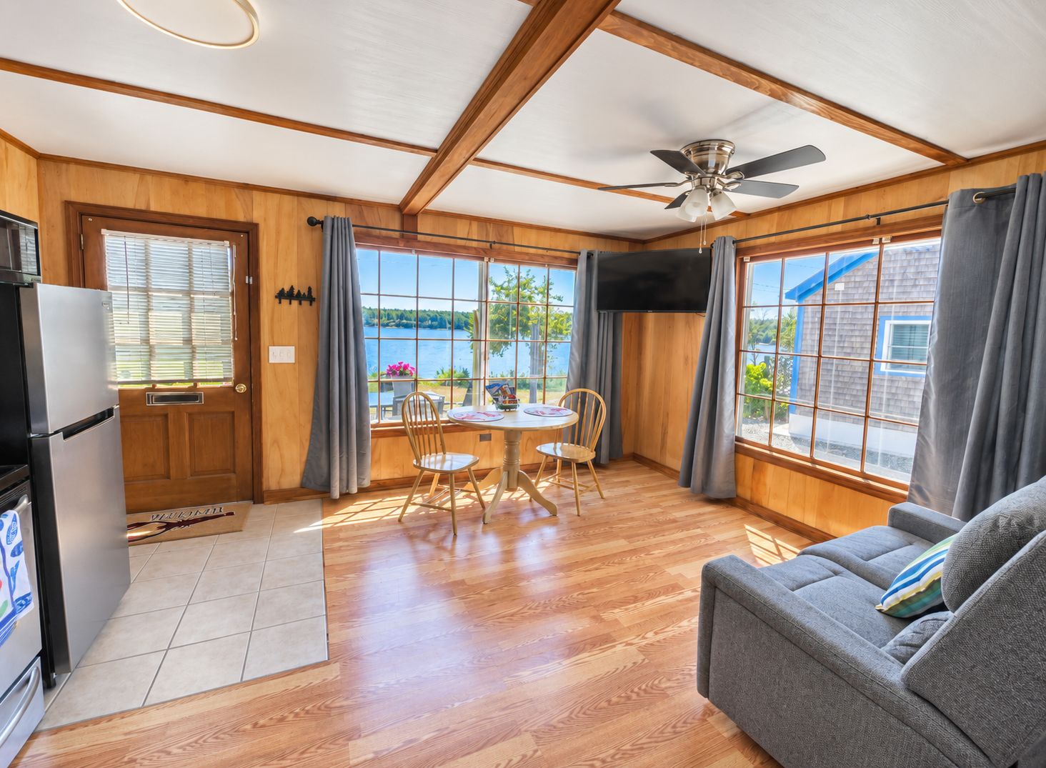 A room with a dining table, chairs, a sofa, a ceiling fan, and a TV.