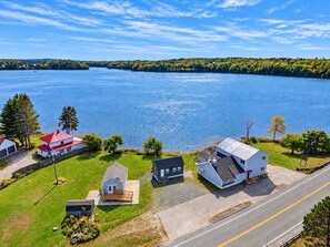 Un quartier résidentiel avec des maisons situées près d’un lac, comprenant une route asphaltée et une zone herbeuse.