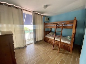 A room with a bunk bed, a wooden dresser, and a sliding glass door leading to a balcony.