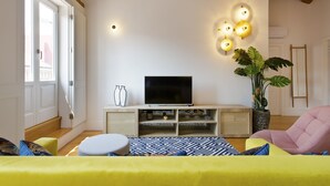 A modern living room with a television, wooden beams, a large plant, and a bright yellow sofa. - Boutique Rentals- The Alma Apt w/balcony (Porto)