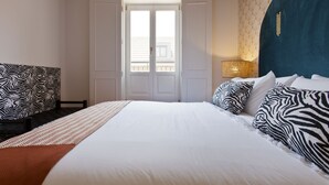 A bedroom with a large bed, zebra-patterned pillows, a wooden headboard, and a window with a view of buildings. - Boutique Rentals- The Alma Apt w/balcony (Porto)