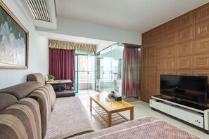 Sala de estar com sofá, mesa de centro, TV em um móvel, porta de vidro que dá para o exterior e painel de parede de madeira.