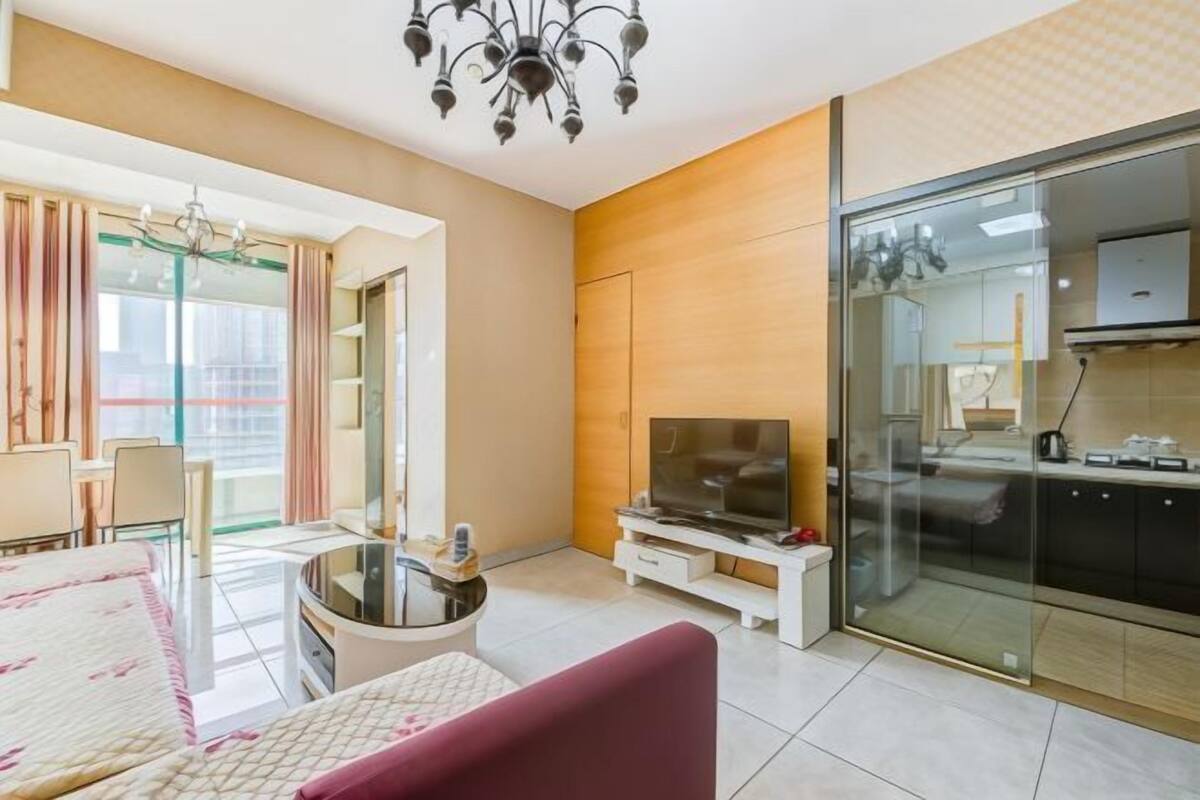 Una sala de estar moderna con televisor, un comedor y una cocina con puerta de vidrio.