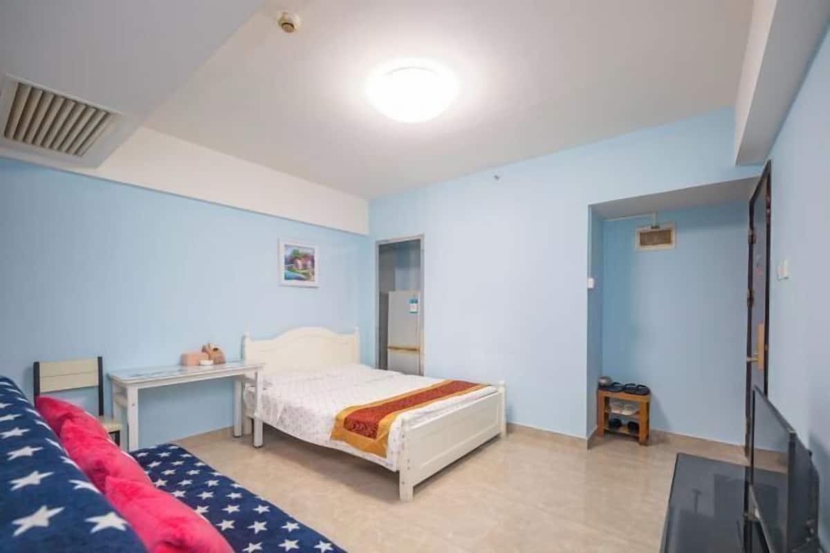 Un dormitorio con cama, escritorio, silla, televisor y puerta que da a otra habitación.