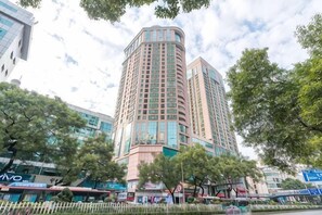 Un edificio alto de varios pisos con fachada curva, rodeado de árboles y otros edificios.