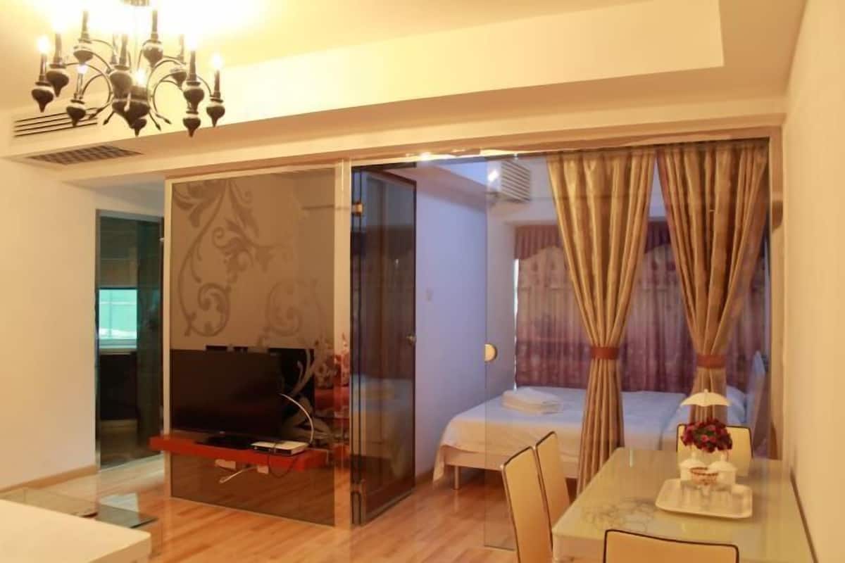 Una habitación con separador de vidrio, una cama, un televisor y un área de comedor con una mesa y sillas.