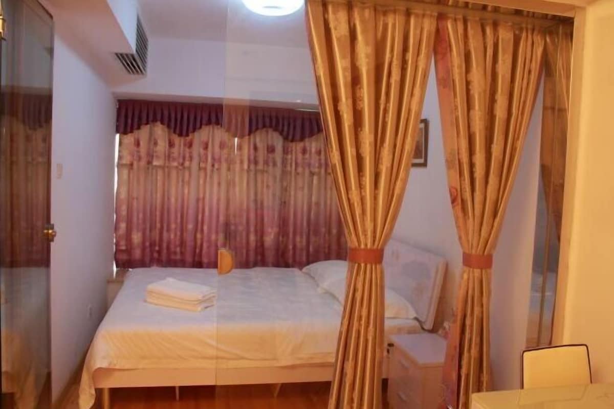 Quarto com cama, cortinas e mesa de cabeceira.