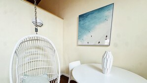 Una habitación con una silla colgante blanca, una mesa blanca y un cuadro en la pared.