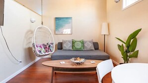 Una sala moderna con un sofá gris, una silla colgante con un cojín colorido, una mesa de centro de madera con un bol de bocadillos y una planta en maceta.