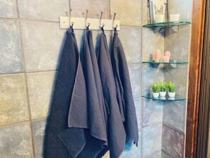 Un bagno con un portasciugamani pieno di asciugamani, uno scaffale in vetro con articoli da toilette e una parete rivestita in piastrelle.