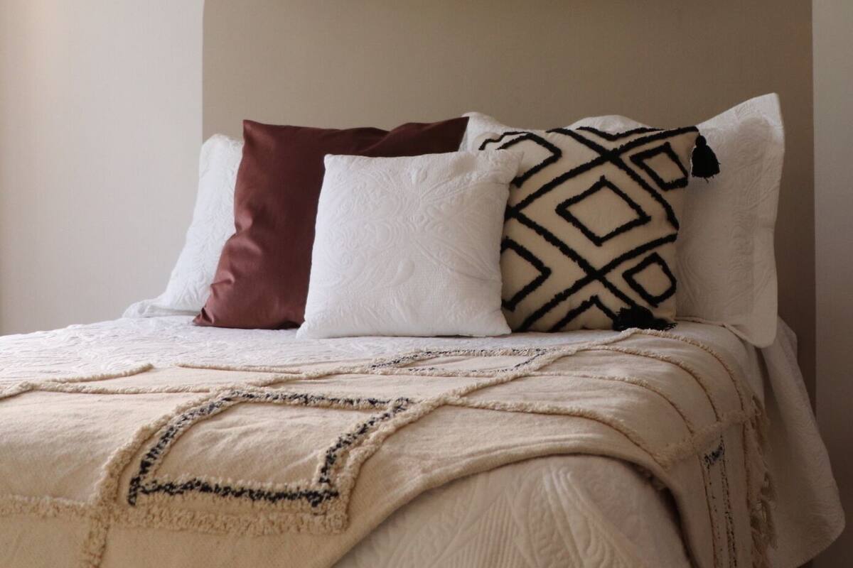 A bedroom with a bed, pillows, a blanket, and a shelf with decorative items.