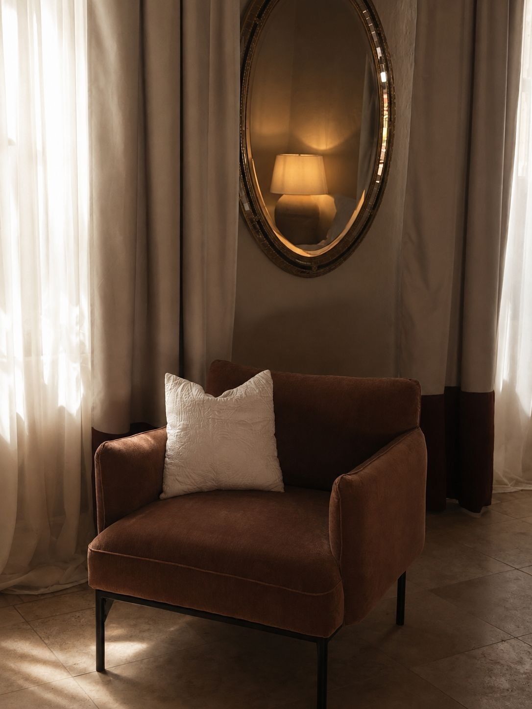 A brown armchair with a white pillow in a room with a large mirror and a lamp on the wall.