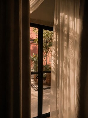 A window with sheer curtains, a view of a courtyard with plants and a building in the background. - Hotel Boutique Casa Damiana (Lagos de Moreno)