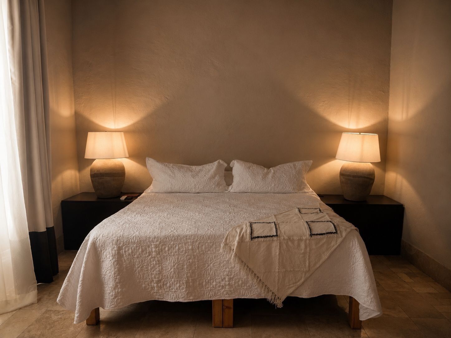 Un lit recouvert d’une couvre-lit blanche et agrémenté de deux lampes de chevet posées sur des tables de nuit en bois.