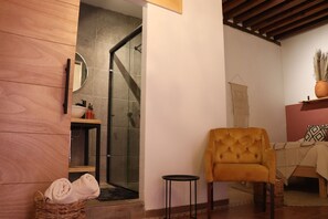A modern bathroom with a glass shower, wooden paneling, a small round table, and a yellow armchair. - Hotel Boutique Casa Damiana (Lagos de Moreno)