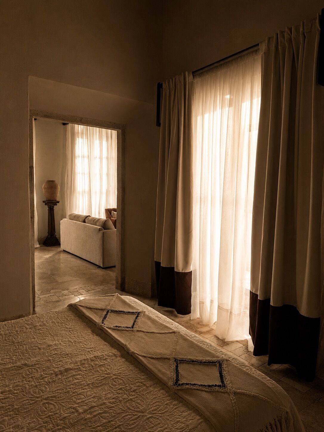 Habitación de hotel con cama, sofá y lámpara. Hay una ventana con cortinas.
