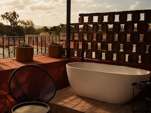 A balcony with a white bathtub, two potted plants, and a wicker chair. - Hotel Boutique Casa Damiana (Lagos de Moreno)
