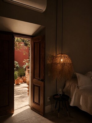 Une pièce intérieure comprenant un lit, une lampe suspendue et donnant sur un espace extérieur agrémenté de plantes en pot.