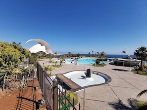 A resort pool area with a central fountain, palm trees, and a distinctive building with a curved roof.
