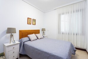 A bedroom with a bed, two bedside tables, a nightstand, a headboard, and two wall-mounted pictures.