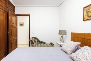 Ein Schlafzimmer mit Bett, Stuhl, Nachttisch, Lampe und Tür.