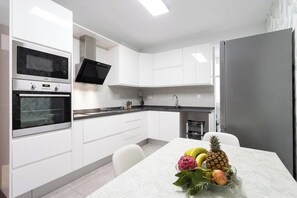 A modern kitchen with white cabinetry, a stainless steel refrigerator, and a microwave.