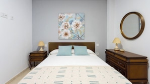 Un dormitorio con cama, dos mesitas de noche, cómoda y espejo, además de una obra de arte floral en la pared.