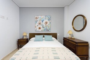 Ein Schlafzimmer mit einem Bett, zwei Nachttischen, einer Kommode, einem Spiegel und einem Blumenbild an der Wand.