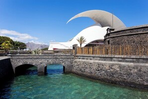 Un puente de piedra sobre aguas claras, un edificio blanco con techo curvo y una pared de piedra con una cerca.