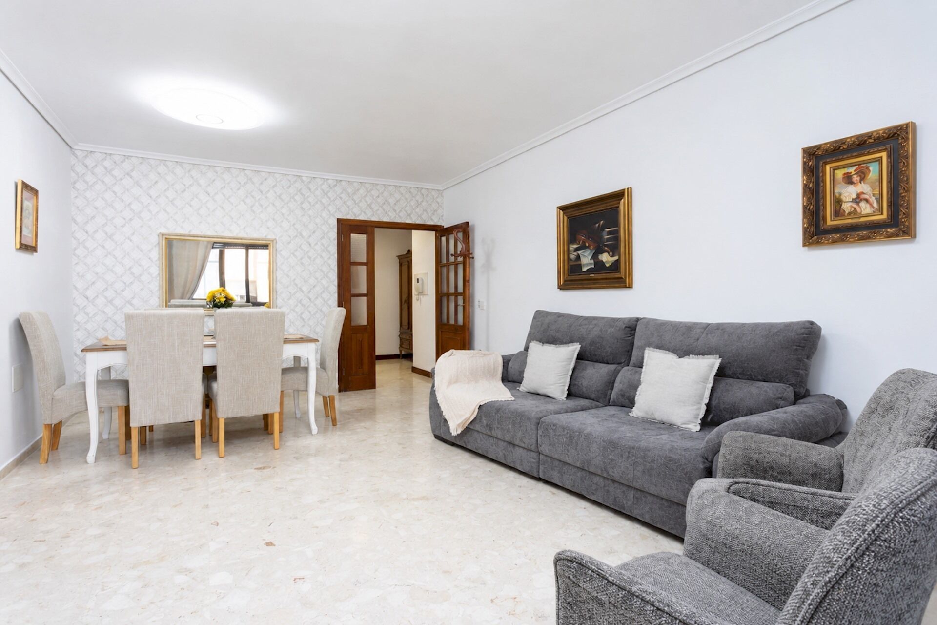Una sala de estar con un sofá gris, una mesa de comedor con sillas y un espejo.