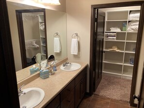Une salle de bain avec deux lavabos, un grand miroir et un dressing avec des étagères.
