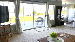 A living room with a large sliding glass door leading to a patio, a wooden coffee table with a plant, and a television on a wooden stand. - Wine Country Getaway with Amazing Views (Kennewick)
