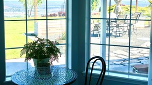 A room with a large window offering a view of an outdoor patio area with a table, chairs, and a potted plant. - Wine Country Getaway with Amazing Views (Kennewick)
