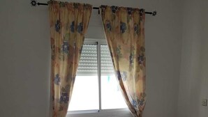 A bedroom with a bed, floral curtains, a window, and two bedside tables. - Nice T3 with terrace - MIXTA residence (Martil)