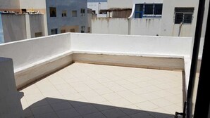 A rooftop terrace with a tiled floor, white walls, and a view of surrounding buildings. - Nice T3 with terrace - MIXTA residence (Martil)
