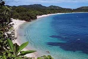 A beach with clear turquoise water, white sand, and lush greenery.