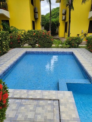 Une piscine rectangulaire aux carreaux de mosaïque bleus, entourée d’une terrasse carrelée et d’une végétation luxuriante.