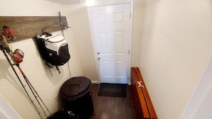 Un pasillo con una puerta blanca, un banco de madera, un bote de basura y un soporte para bicicletas en la pared.