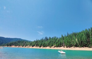 A boat anchored near a forested shoreline with clear blue water. - Tranquil Updated Mill House with backup power and hi speed Wifi! (McCloud)