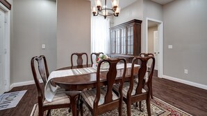 Un comedor con una mesa y sillas de madera, una araña y un aparador al fondo.